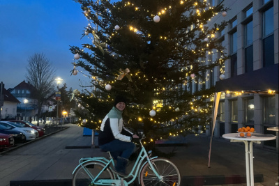 Person auf einem Fahrrad vor einem beleuchteten Weihnachtsbaum. Mithilfe des Fahrrades kann Strom für die Beleuchtung des Weihnachtsbaums erzeugt werden.