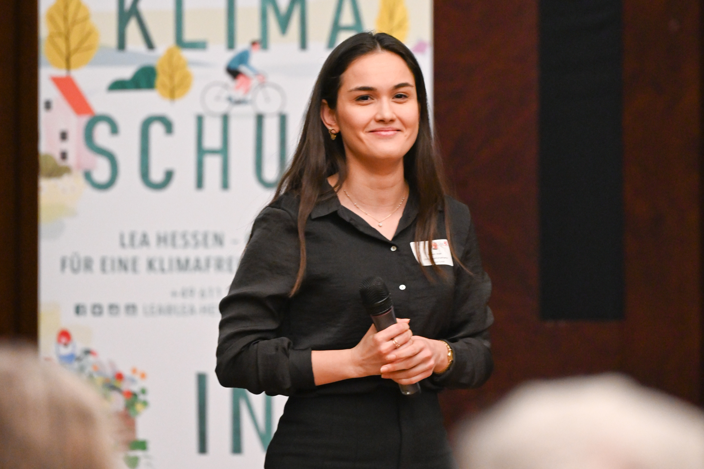 Regionaltreffen IEEKN 2023: Junge Frau steht vor Publikum, im Hintergrund ein Klimaschutzposter.