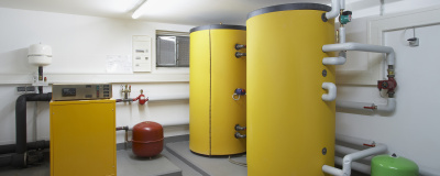 Kellerraum mit Elementen eines Heizpumpensystems für Erdwärme: zwei gelbe, zylindrische Wasserbehälter und ein gelber Reglerkasten.